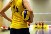 A volleyball player holds a ball, other volleyball players can be seen in the background